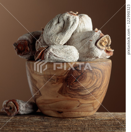 Dried persimmons in a wooden dish on a brown background. 122998323