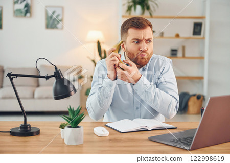 Holding the fruit. Man with banana sitting by the table with laptop on it and have fun Holding the fruit. Man with banana sitting by the table with laptop on it and have fun 122998619