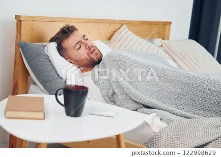 Sick man laying down on the bed at home and feels bad. Conception of self isolation 122998629