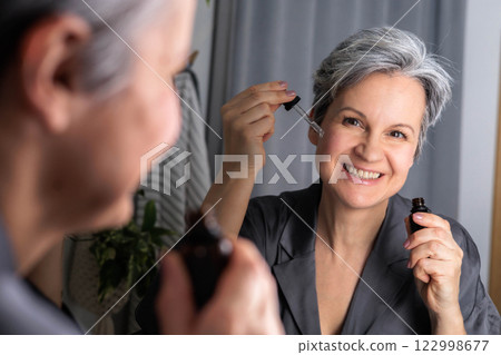 An adult beautiful woman of age during menopause with gray hair applies hormonal serum 122998677