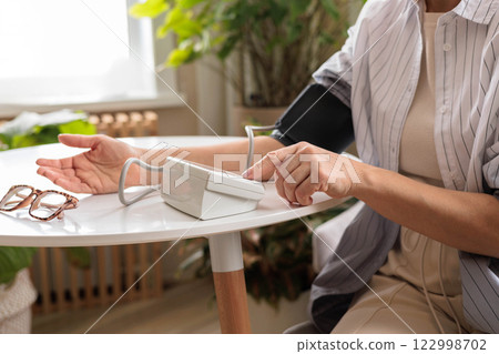 A woman in a blue shirt measures her blood pressure with a tonometer on a white table. 122998702
