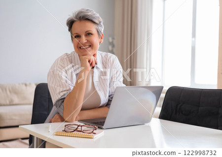 Beautiful elderly woman pensioner businesswoman with gray hair works on computer remotely  122998732