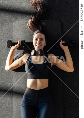 Strong beautiful fitness woman training back doing exercise with dumbbells at gym. 122998746