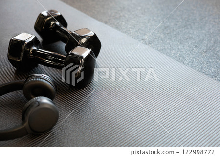 Headphones and black dumbbells lie on a black yoga mat. Flat lay. Space for text. 122998772