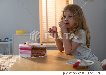 A child is joyfully enjoying a delicious cake while sitting in a cozy and warm room 122998916