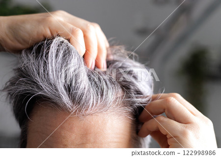 An adult woman of age with gray hair examines in front of the mirror the amount of gray hair on head An adult woman of age with gray hair examines in front of the mirror the amount of gray hair on head 122998986