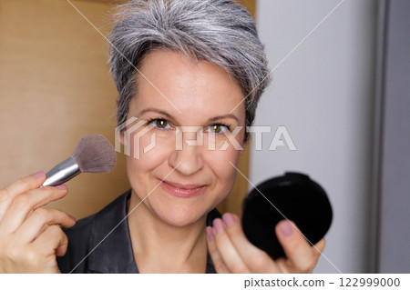 Beautiful smiling elderly woman pensioner during menopause with gray hair applies anti-aging makeup Beautiful smiling elderly woman pensioner during menopause with gray hair applies anti-aging makeup 122999000