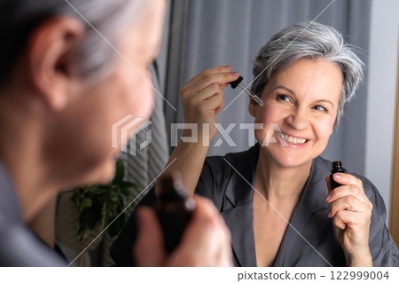 An beautiful woman of age during menopause with gray hair applies hormonal serum against wrinkles An beautiful woman of age during menopause with gray hair applies hormonal serum against wrinkles 122999004
