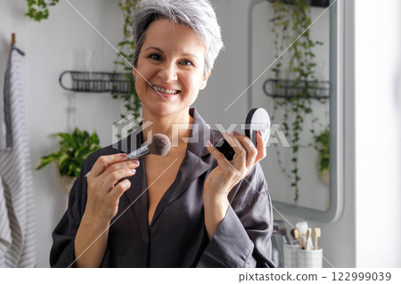 Beautiful smiling elderly woman pensioner during menopause with gray hair applies anti-aging makeup Beautiful smiling elderly woman pensioner during menopause with gray hair applies anti-aging makeup 122999039