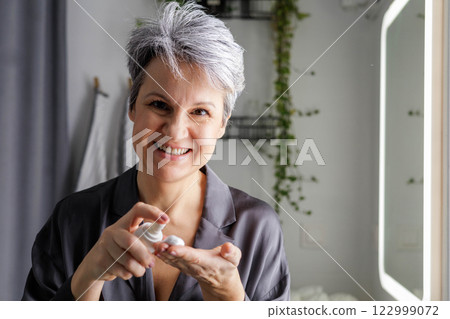 Mature beautiful woman during menopause with gray hair applies hormonal anti-aging cream 122999072
