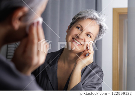 Mature well-groomed beautiful woman during menopause with grey hair removes daytime makeup Mature well-groomed beautiful woman during menopause with grey hair removes daytime makeup 122999122