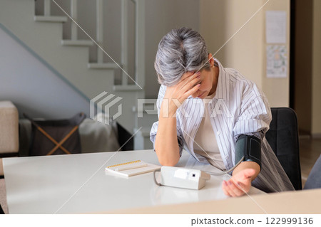 A woman at home tries to fight migraine and headache and measures blood pressure with a tonometer 122999136