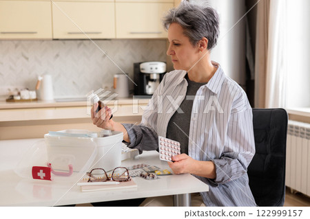 Beautiful aged woman pensioner aged with gray hair checking medicines at domestic first aid kit. Beautiful aged woman pensioner aged with gray hair checking medicines at domestic first aid kit. 122999157