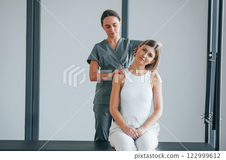 Neck exercises. Woman is in health center getting help by doctor Neck exercises. Woman is in health center getting help by doctor 122999612