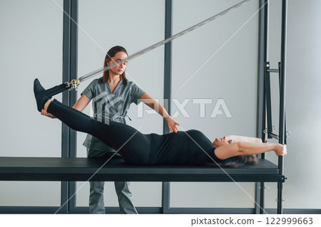Legs is on the stretching cable. Woman is in health center getting help by doctor Legs is on the stretching cable. Woman is in health center getting help by doctor 122999663