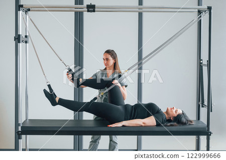 Legs is on the stretching cable. Woman is in health center getting help by doctor Legs is on the stretching cable. Woman is in health center getting help by doctor 122999666