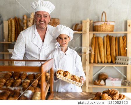 Father baker poses with his young daughter who helps sell fresh bread at bakery 123002553