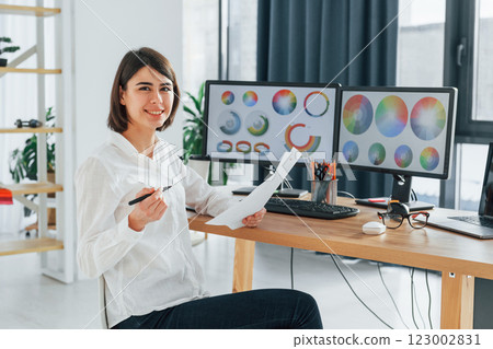 With paper. Female designer working in the office by using PC With paper. Female designer working in the office by using PC 123002831