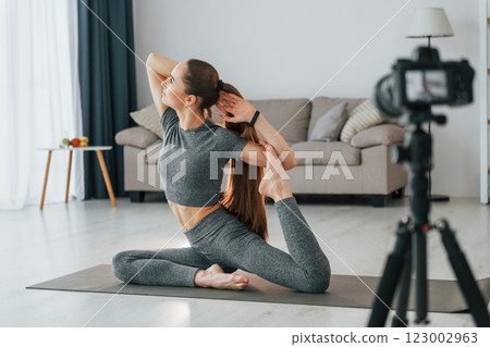 Doing lessons on camera. Young woman with slim body type and in yoga clothes is at home Doing lessons on camera. Young woman with slim body type and in yoga clothes is at home 123002963