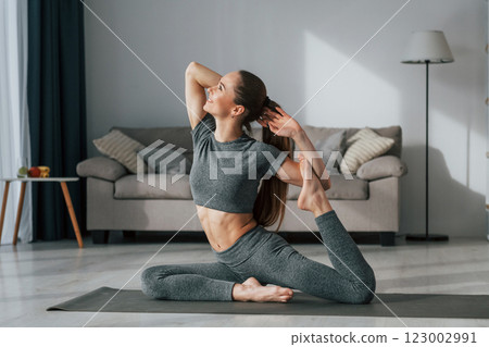Stretching the legs. Young woman with slim body type and in yoga clothes is at home 123002991