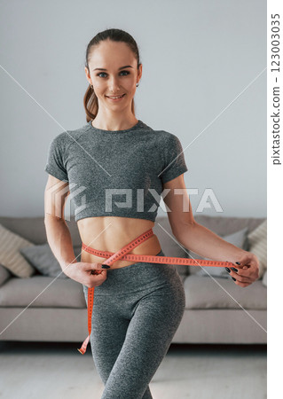 Concept of dieting. Young woman with slim body type and in yoga clothes is at home Concept of dieting. Young woman with slim body type and in yoga clothes is at home 123003035