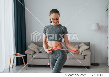 Standing in domestic room. Young woman with slim body type and in yoga clothes is at home 123003036