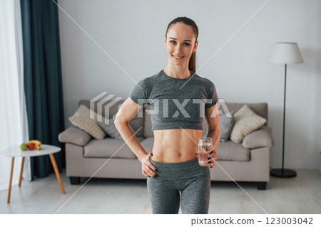 With glass of water. Young woman with slim body type and in yoga clothes is at home 123003042
