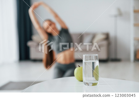 With glass of water. Young woman with slim body type and in yoga clothes is at home With glass of water. Young woman with slim body type and in yoga clothes is at home 123003045