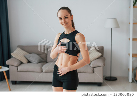 In black sportive clothes. Young woman with slim body type is at home 123003080