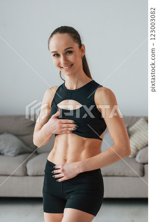 In black sportive clothes. Young woman with slim body type is at home 123003082
