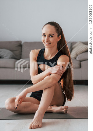 Sitting and smiling. Young woman with slim body type and in yoga clothes is at home 123003102