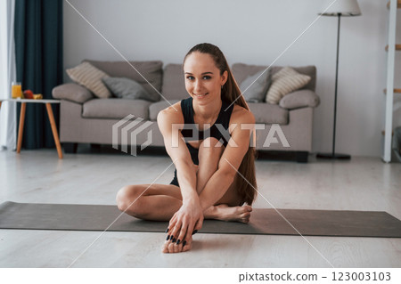 Sitting and smiling. Young woman with slim body type and in yoga clothes is at home Sitting and smiling. Young woman with slim body type and in yoga clothes is at home 123003103