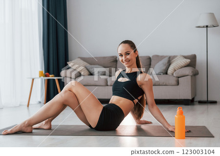 Sitting and smiling. Young woman with slim body type and in yoga clothes is at home Sitting and smiling. Young woman with slim body type and in yoga clothes is at home 123003104