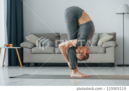 Big stretches. Young woman with slim body type and in yoga clothes is at home Big stretches. Young woman with slim body type and in yoga clothes is at home 123003119