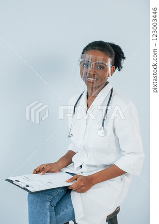 Sitting and holding notepad. Young african american woman is against white background 123003446