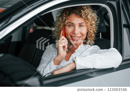 Using phone. Woman with curly blonde hair is in autosalon Using phone. Woman with curly blonde hair is in autosalon 123003586
