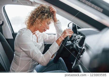 Side view. Woman with curly blonde hair is in autosalon 123003595
