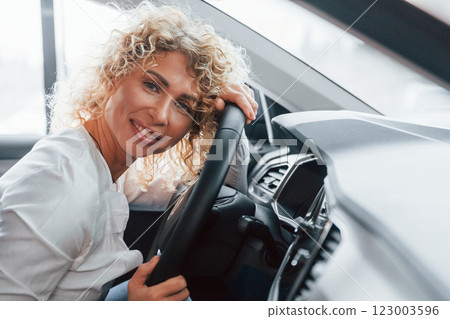 Side view. Woman with curly blonde hair is in autosalon 123003596