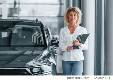 Holding notepad. Woman with curly blonde hair is in autosalon 123003621