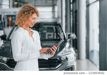 In official white shirt. Woman with curly blonde hair is in autosalon 123003692