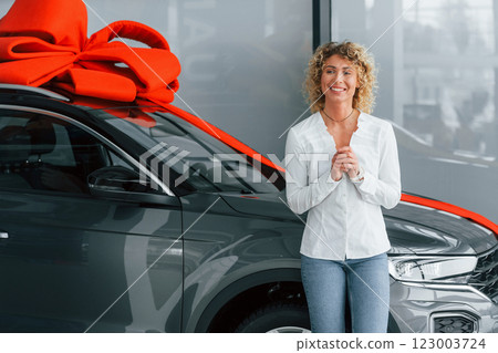 Expensive gift. Woman with curly blonde hair is in autosalon 123003724