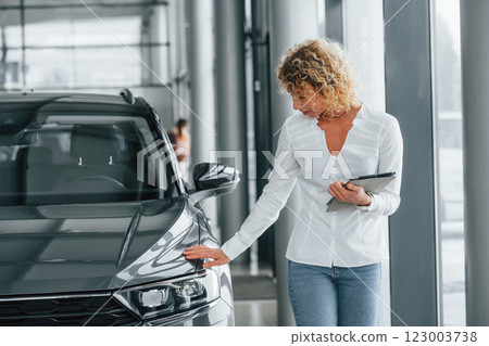 Tablet is in the hands. Woman with curly blonde hair is in autosalon Tablet is in the hands. Woman with curly blonde hair is in autosalon 123003738