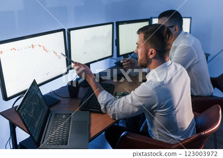 Analizing graphs together. Two stock traders working in the office with exchange technology Analizing graphs together. Two stock traders working in the office with exchange technology 123003972