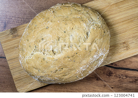 Top view of baked semi-circular loaf of homemade bread on narrow bamboo wood cutting board on kitchen countertop with artificial wood grain. Cooking at home, the concept of home, comfort Top view of baked semi-circular loaf of homemade bread on narrow bamboo wood cutting board on kitchen countertop with artificial wood grain. Cooking at home, the concept of home, comfort 123004741