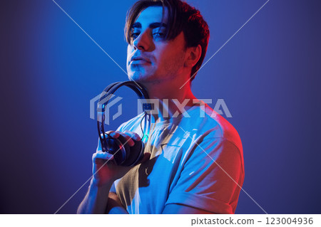 Holding headphones in hands. Man standing in the studio with neon light 123004936