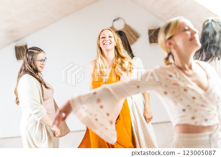Group of cheerful women all ages, happy people dancing together wearing traditional colorful dresses and hippy clothes. Free people enjoying leisure activity, emphasizing friendship, fun, movement. 123005087
