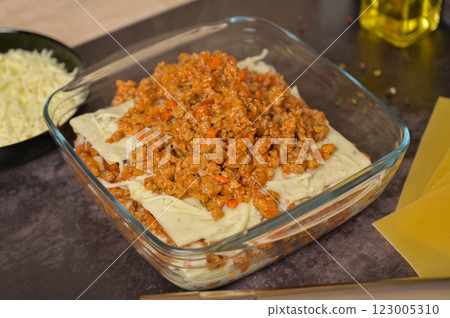 Bolognese sauce in a glass form. Lasagne pasta sheets. Grated cheese in a black bowl. Black background. Homemade lasagna cooking preparation 123005310