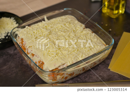 Homemade lasagna cooking preparation. Grated cheese, Bolognese sauce in a glass form. Lasagna pasta sheets. Cheese in a black bowl. Black background 123005314