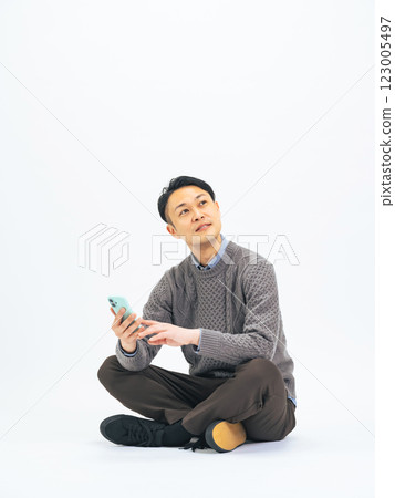 一位身著休閒裝的中年男子坐著使用智慧型手機的全身照片 123005497
