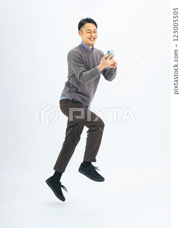 Full-body photo of a middle-aged man in casual wear jumping while looking at his smartphone Full-body photo of a middle-aged man in casual wear jumping while looking at his smartphone 123005505